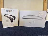 Photo showing boxed Muse2 Meditation Headband and SUNmini Plus UV LED Lamp side by side on the floor with beige wall background.