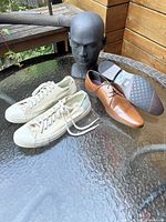 Photo showing the Topman brown leather dress shoes and Converse white canvas sneakers on glass table with mannequin head.
