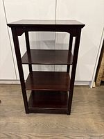 Front view of the traditional dark brown wooden display shelf showing three shelves and supporting legs.