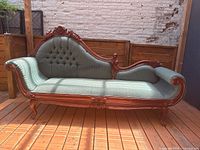 Full view of the antique Victorian sofa placed outdoors on wooden deck. Shows carved wooden frame and green upholstery with bouton tufting.