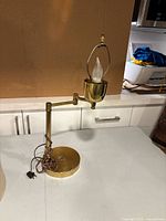 Front angle view of vintage adjustable metal table lamp with round weighted base, adjustable arm with multiple joints, flame bulb holder, and original brown cord and plug coiled on base.