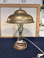 Front angled view of the vintage bronze metal table lamp with dome shaped shade, vertical column and round base with electrical cord coiled on base.