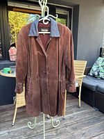 Front view of brown suede jacket with leather collar and button closure hanging on stand