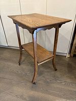 Side angled view of the vintage oak table showing wood grain, scalloped edges, and wheels on legs.