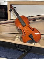 Violin displayed inside open protective case showing wood finish and black fingerboard