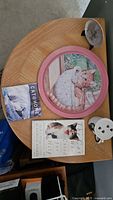 All items on table: round cat tray, two books, mug with lid, metal display stand edge visible