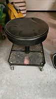 Black round rolling stool with vinyl seat, metal base tray and casters