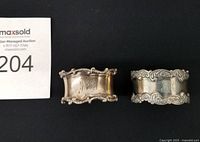 Front view of both Birks sterling napkin rings showing scroll borders and monograms