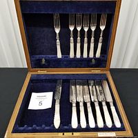 Open oak case showing six knives and seven forks inside blue velvet slots