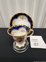 Cup positioned in front of saucer showing cobalt rim, gold scrollwork, floral centre