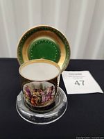 Cup in front of saucer, showing front figural scene and green-gold interior of saucer