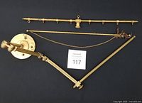 Three brass hardware pieces laid out: articulated wall bracket, rod with rings, rod with chain