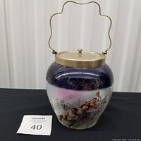 Full view of porcelain biscuit barrel showing cobalt band, winter scene, brass lid and handle