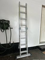 Full view of the aluminum ladder set up in leaning position against a white wall showing overall height and structure.