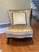 Front view of beige velvet accent chair with matching fringed square pillow on wooden floor