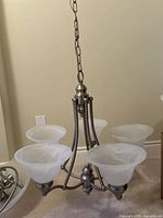 Top view showing the five frosted glass shades attached to the brushed nickel frame with a central decorative fixture and suspension chain.