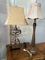 Full view of two ornate table lamps on wooden table with visible cords and lamp shades.