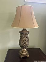 Single ornate Ashley Furniture table lamp with intricate carved base and tan fabric shade