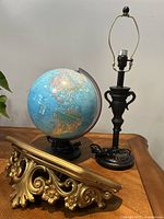 Set showing black metal lamp base, blue illuminated globe, and ornate gold decorative shelf base