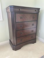 Front view of the chest showing five drawers, dark brown finish, fluted corner details, and decorative metal ring pulls.