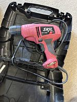 Top view of red Skil electric drill placed inside the black plastic carrying case, displaying the drill, cord, and case interior.