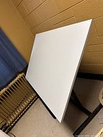 Photo showing white flat drafting table surface from an angled top view reflective of the desk's color and size.