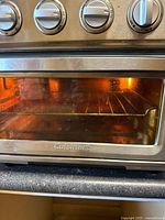 Front view of the stainless steel Cuisinart toaster oven showing the glass door, interior light on, wire rack inside and visible brand mark on door.
