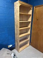 Photo of a blonde wooden bookcase showing four shelves, some adjustable and some fixed, next to a wooden door and blue wall.