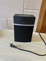 Front and side view of black Bose SoundTouch speaker on table with power cord.
