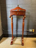 Full front view of the polished wooden gentleman's valet stand showing the top hanger, drawer, legs, and base bars