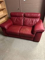 Front view of a red leather loveseat showing slight discoloration and wear on seating area and armrests.
