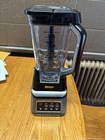 Front view of Ninja blender with clear plastic 72 oz blending jar on silver and black base on wooden table.