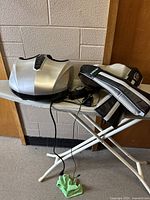 Full view of Belmint foot massager device on a small folding table with truMedic neck and shoulder massager placed alongside it, power cords visible.