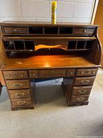 Front view of the oak roll top desk showing the top small drawers, pigeon holes, roll top surface with built-in light, and lower drawers.