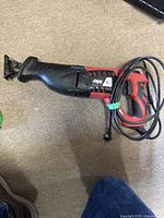 Side view of black and red Skil reciprocating saw showing trigger, handle, and cord wrapped with green twist tie.