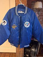 Full front view of Chalk brand royal blue satin bomber jacket on hanger showing embroidered patches and striped rib knit trim