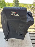 Grill covered with black Weber SmokeFire branded protective cover