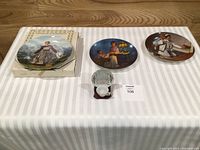 All three collector plates, miniature teacup, saucer and stand displayed on table