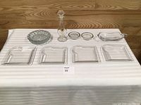 All nine pieces laid out: four plates, ashtray, two small dishes, butter dish, decanter with stopper