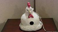 Frontal view of the white ceramic chicken bird house showing the entrance hole, red comb and wattles, and textured nest base.