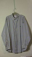 Full view of Brooks Brothers men's polo shirt with blue and yellow checkered pattern on white, button-down collar, and buttons on cuffs, hanging on a hanger.