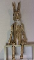 Front view of the carved wooden articulated rabbit figurine with long ears and jointed limbs, seated on a shelf.