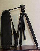 Full view of the black Celestron tripod standing with its legs extended and foam grip visible on one leg with the black carrying bag beside it.