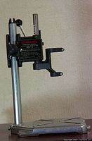Front view of Dremel deluxe drill press stand showing base, vertical post, tool holder and clamp.