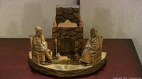 Full view of the carved wooden sculpture showing a man and woman seated on either side of a stone fireplace with a dog and cat in the center.
