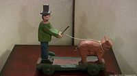 Front view of the folk art wooden sculpture showing man with pig on leash on wheeled platform.