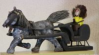 Side view of the folk art wooden horse pulling a sleigh with a figure dressed in winter clothing.