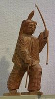 Side view of the wooden folk art carving showing hunter holding bow and arrow with snowshoes.