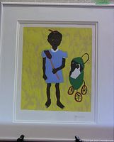 Framed print showing a girl in a blue dress holding a fly swatter, next to a doll carriage with a doll inside, all against a yellow background. Print is signed.