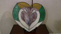 Leaded glass sun catcher shaped like a heart with two swans facing each other inside. Multicolored glass with prominent green, white, purple, and yellow sections.